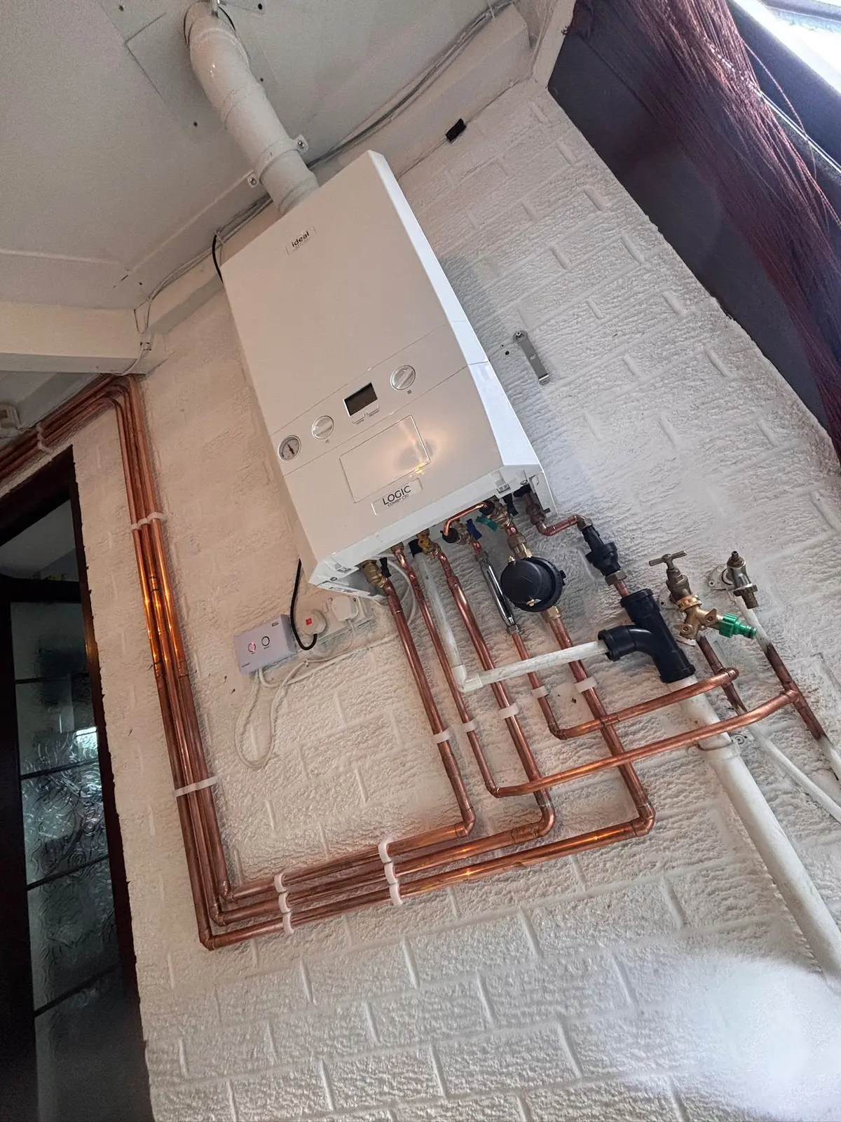 Ideal Logic combi boiler with long runs of clipped copper pipework across a white brick-effect wall
