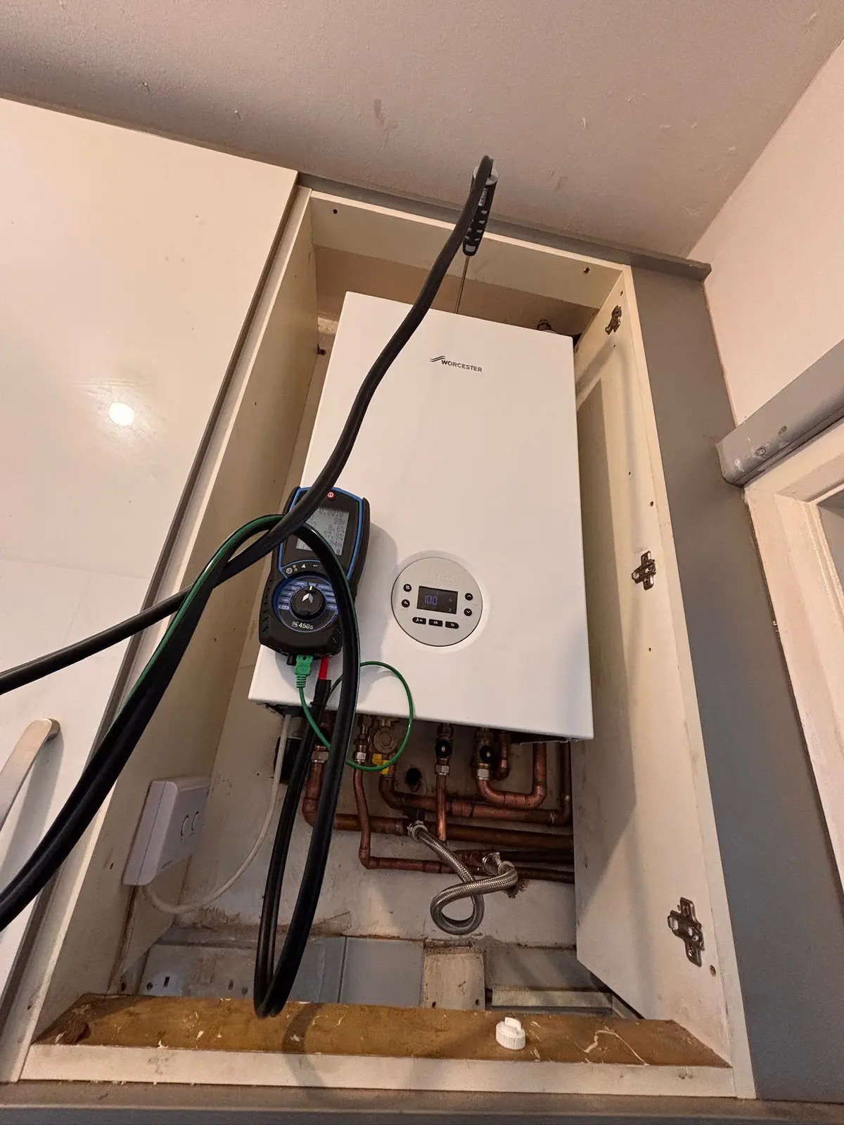 Worcester Bosch boiler inside a kitchen cupboard being commissioned with a flue gas analyser