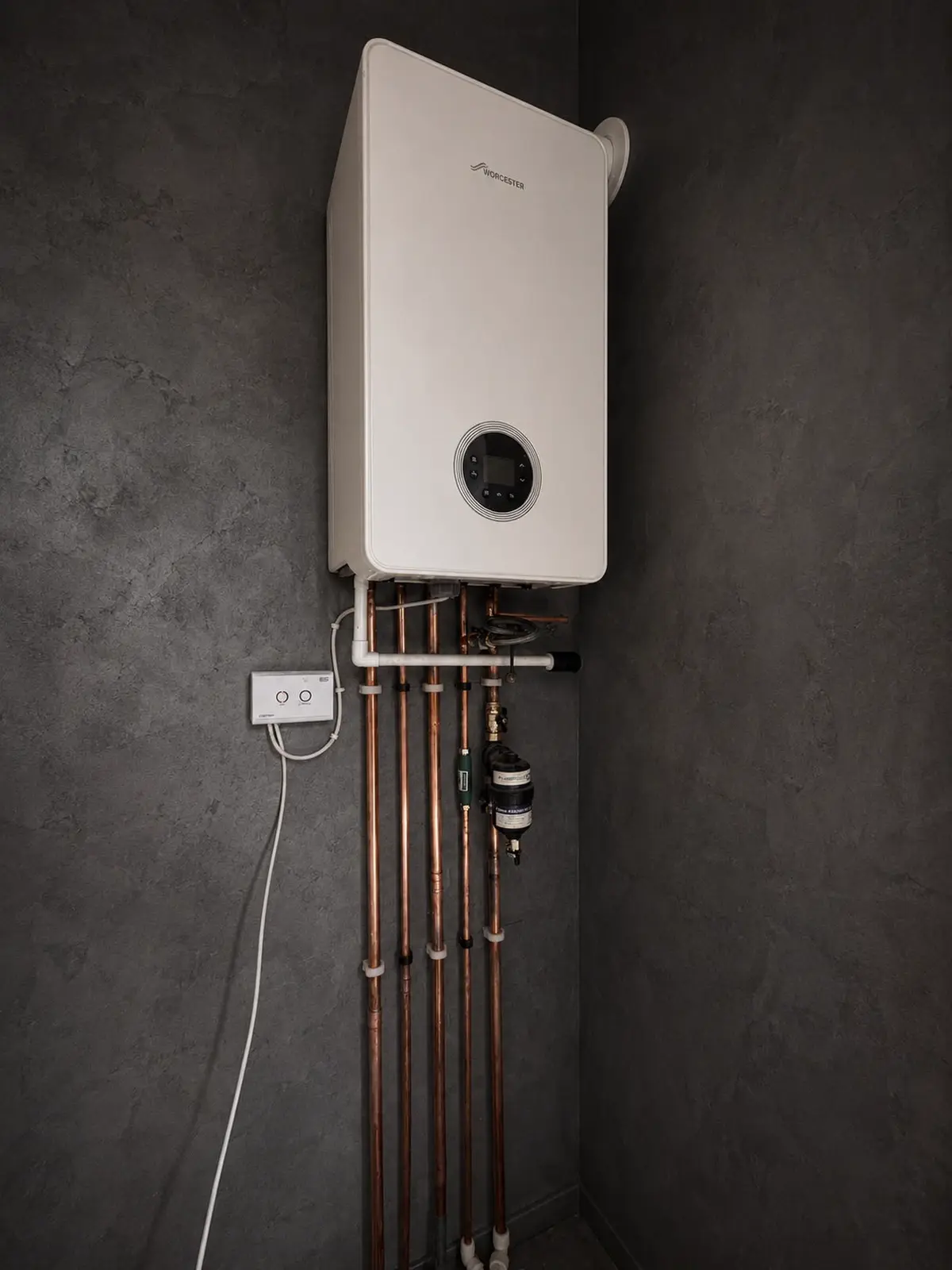 Worcester combi boiler fitted on a dark grey wall above five clipped copper pipe runs, an inline filter and a wall-mounted controller