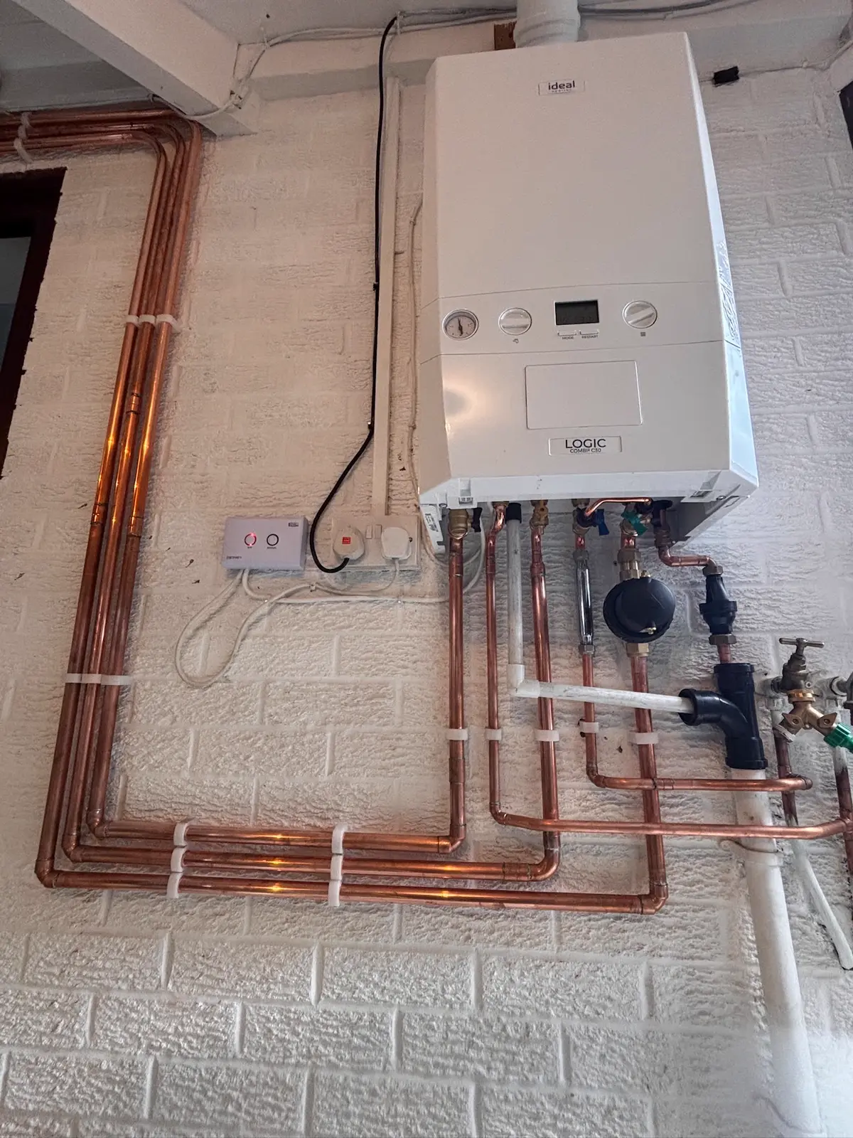 Ideal Logic boiler with long copper heating runs clipped around a white brick wall and down to floor level