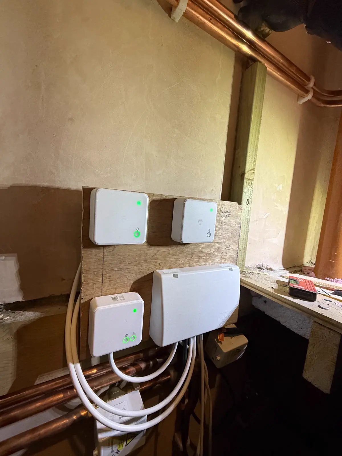 Three heating wiring centres with lit power indicators mounted on a board below the copper pipework