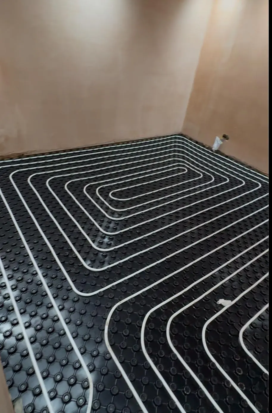 White underfloor heating pipe clipped into black castellated floor panels in evenly spaced loops